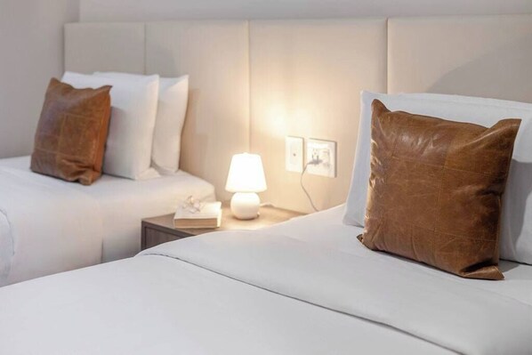 A hotel room with two beds, a nightstand with a lamp, and a headboard.