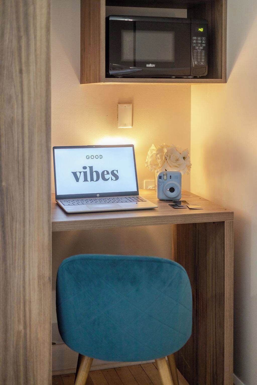 A laptop on a desk with a 'vibes' sign, a camera, and a microwave above.