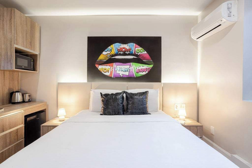 Camera d'albergo con un letto, lampade sui comodini, forno a microonde, macchina del caffè e condizionatore d'aria a parete.