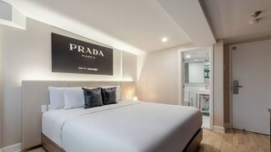 Una habitación de hotel moderna con una cama grande, un letrero de Prada en la pared y un baño visible a través de una puerta abierta.