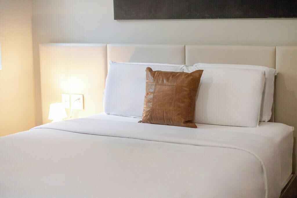 Una cama bien hecha con sábanas blancas y una única almohada marrón.