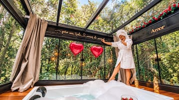 Un cuarto de spa con una bañera grande, un box de ducha de vidrio y vistas a árboles por las ventanas.