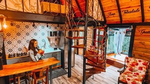Un intérieur chaleureux avec un plafond en bois, un coin repas comprenant un banc et une table, un escalier et un canapé recouvert d’un tissu à motifs floraux.