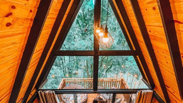 Une cabane en bois dotée d’une grande fenêtre, d’un escalier et d’un intérieur chaleureux.