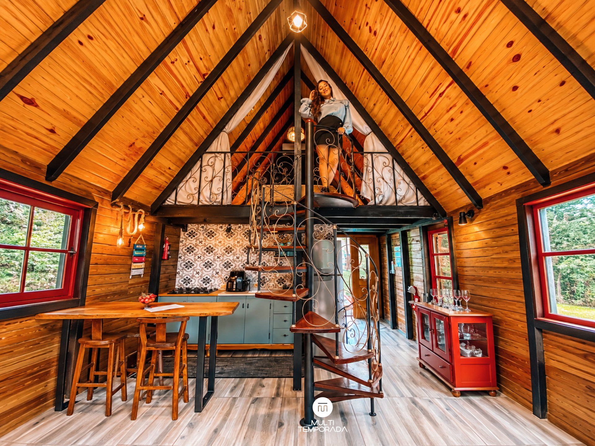 A cozy cabin interior with a wooden interior, a dining area, a kitchen, and a spiral staircase.