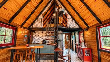 A cozy cabin interior with a wooden interior, a dining area, a kitchen, and a spiral staircase.