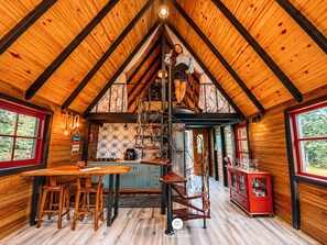 A cozy cabin interior with a wooden interior, a dining area, a kitchen, and a spiral staircase. - Recanto Bellavita - Rancho Queimado - SC (Rancho Queimado)