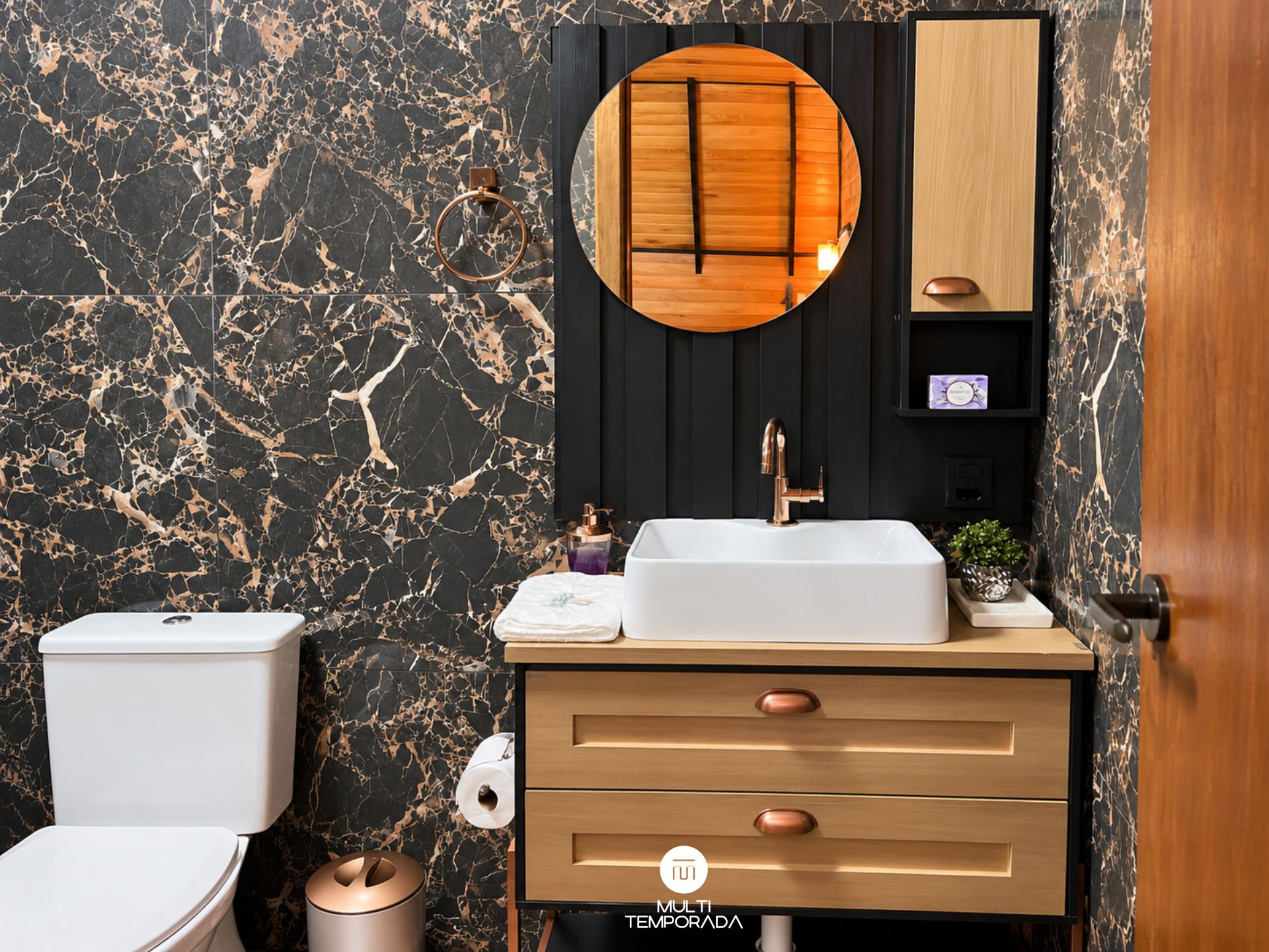 A bathroom with a marble wall, a wooden vanity, a white sink, and a toilet.