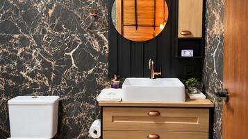 A bathroom with a marble wall, a wooden vanity, a white sink, and a toilet.