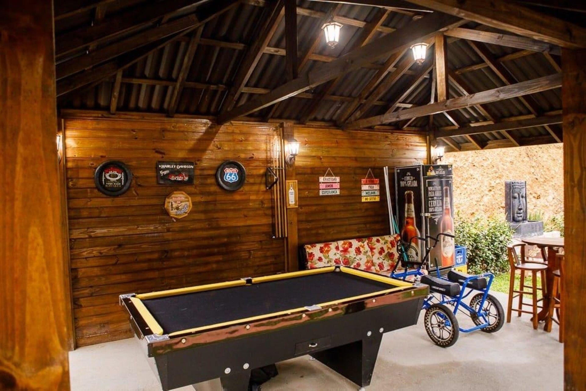 A pool table in a rustic room with wooden walls, a ceiling with exposed beams, and a wheelchair in the corner.