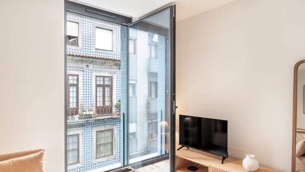 En moderne stue med et stort skydedørsparti, der fører ud til en balkon, et fladskærms-tv på et træpanel og en hvid vase på panelet.
