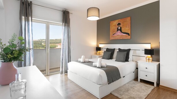 A modern bedroom with a large bed, bedside tables, a nightstand, a potted plant, and a painting on the wall. - Óbidos Pool & Charm - Pet Friendly (Óbidos)