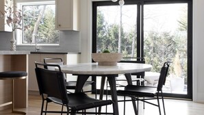 Une cuisine moderne avec un coin repas, dotée d’une grande fenêtre, d’un luminaire suspendu et offrant une vue sur l’extérieur.