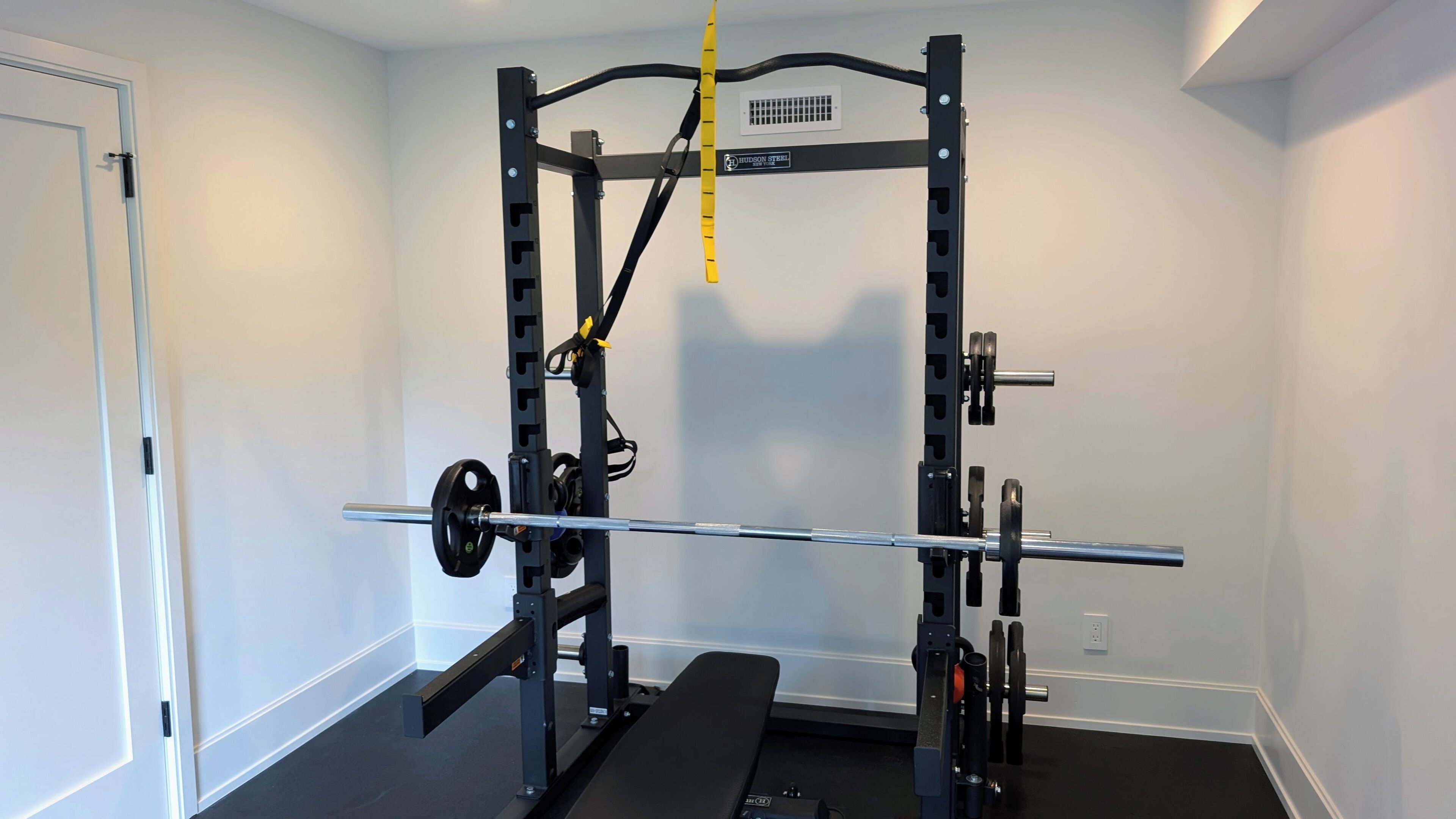 A home gym with a squat rack, bench, and weight plates.