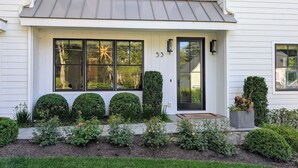 Une maison blanche avec une porte noire, le numéro 53, et une grande fenêtre ornée d’un luminaire en forme d’étoile.