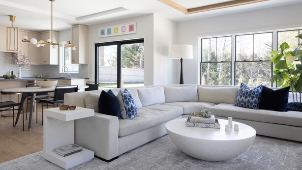Un salon moderne avec un grand canapé en forme de L, une table basse ronde et un coin repas comprenant une table et des chaises blanches.