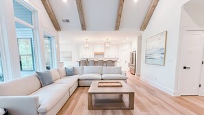 A modern living room with a sectional sofa, a coffee table, and a kitchen in the background. - Luxury Lake Home on Golf Course (Waleska)
