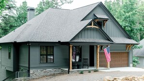 A two-story house with a stone foundation, a dark gray roof, and a front porch with a bench. - Luxury Lake Home on Golf Course (Waleska)