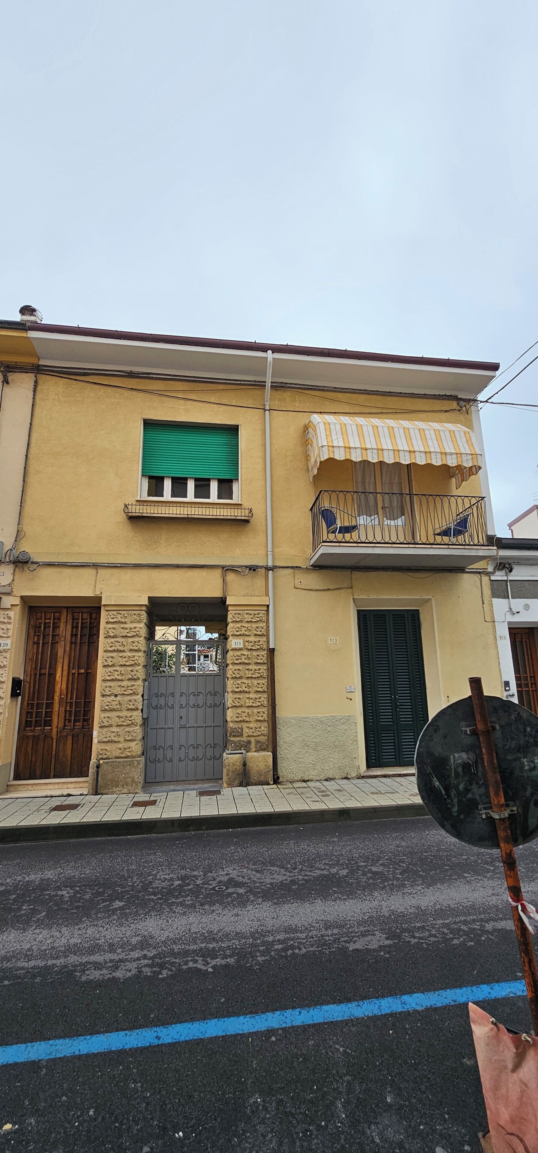 A two-story building with a balcony, a green shuttered window, and a gated entrance.