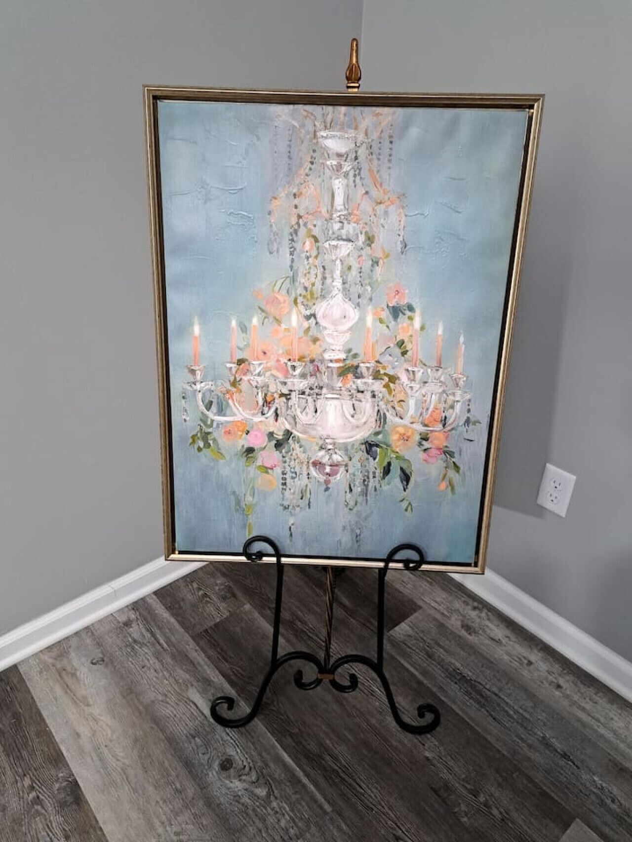 A framed painting of a chandelier with flowers on a stand in a corner.