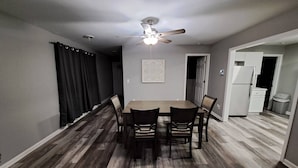Un comedor con mesa y sillas, un ventilador de techo y una cocina al fondo.