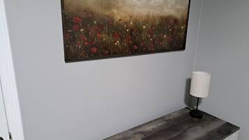 A room with a wooden bench, a painting of a field with flowers, and a lamp on the bench.