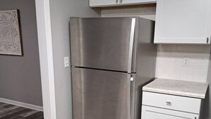 Una cocina con un refrigerador de acero inoxidable, armarios blancos y piso de madera.
