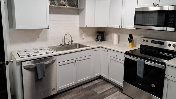 Una cocina moderna con armarios blancos, un microondas de acero inoxidable, horno integrado y cafetera.