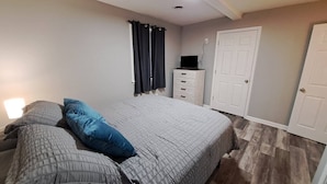 Un dormitorio con cama, cómoda, televisor y puerta.