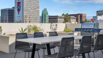 An outdoor patio with a grill, seating, and a view of city buildings.