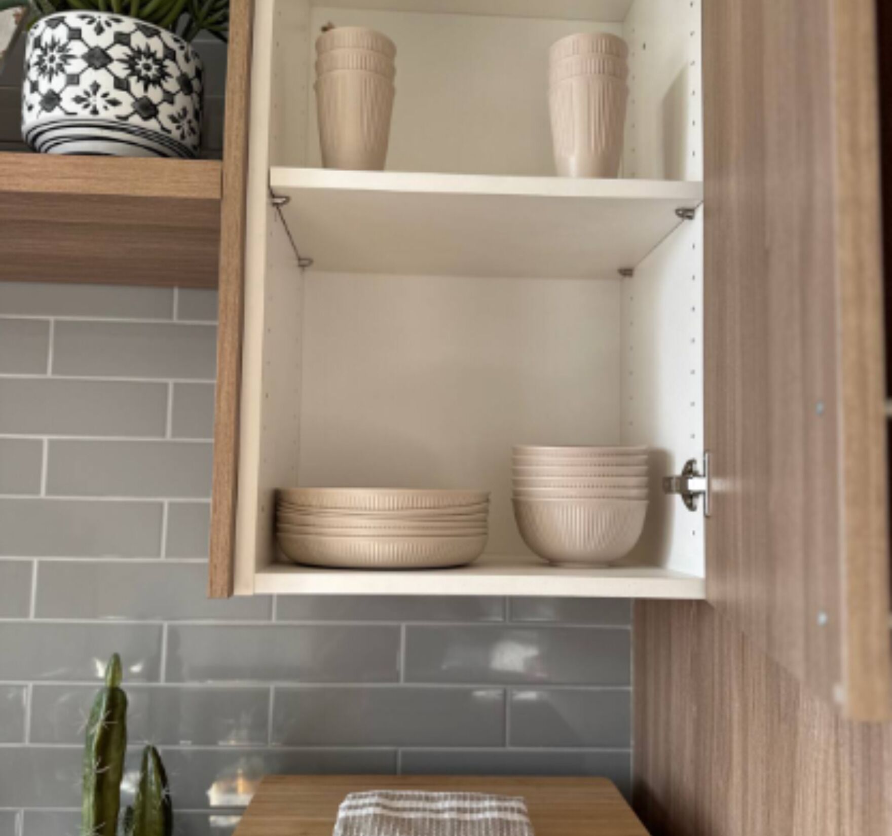 A kitchen cabinet with two shelves, one with a decorative pot and the other with stacked bowls.