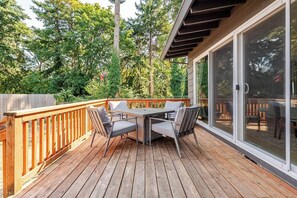 Une terrasse en bois avec une table et des chaises, entourée d’une balustrade en bois et de portes coulissantes en verre.