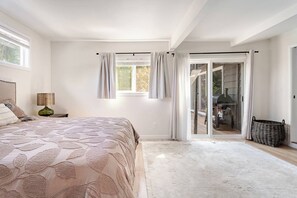 Une chambre avec un grand lit, une table de chevet, une lampe et une vue sur un patio équipé d’un barbecue.