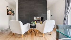Un salon moderne avec deux fauteuils blancs, une table basse en verre et une cheminée en arrière-plan.