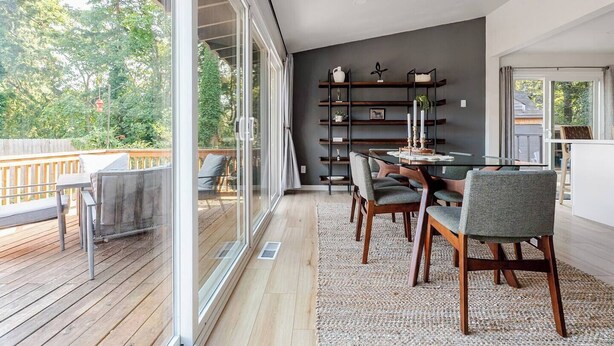 Un espace repas moderne avec un mur en verre, une terrasse en bois et un mur d’accent de couleur foncée.