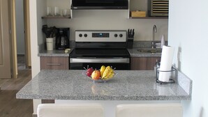 Una cocina moderna con una isla central, dos taburetes de bar, horno empotrado y fregadero.