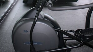 Un gimnasio con bicicletas estáticas y una cinta de correr, amplias ventanas con vistas a un parque y edificios.