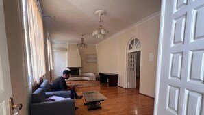 A spacious living room with a wooden floor, a sofa, a coffee table, and a chandelier. - Trippoo Villa & Hostel (Baku)