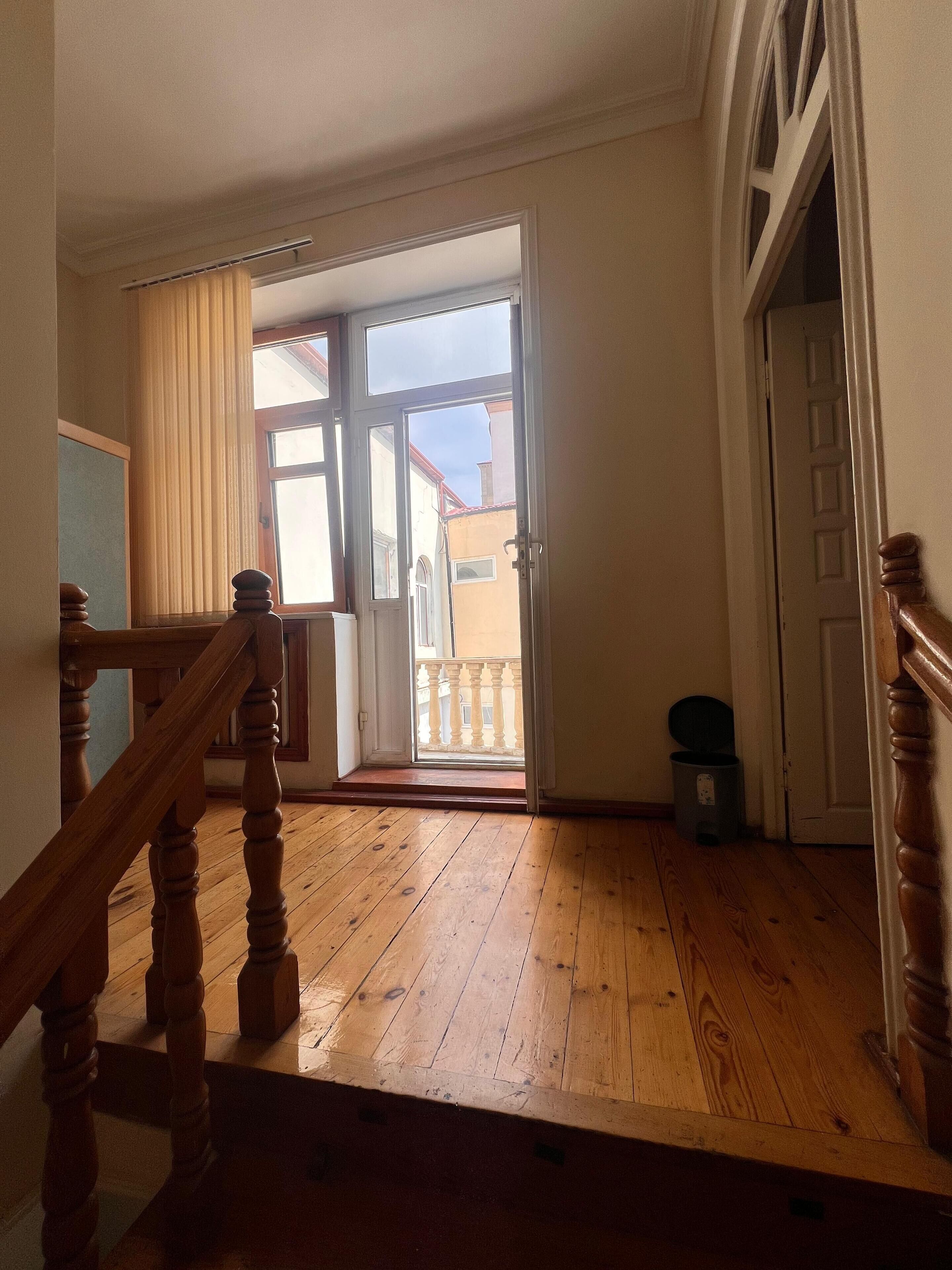 Una habitación con piso de madera, una escalera con barandilla de madera y una puerta que da al exterior.