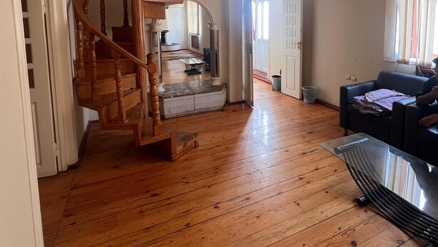 A spacious living room with a wooden staircase, a glass coffee table, and a black sofa. - Trippoo Villa & Hostel (Baku)