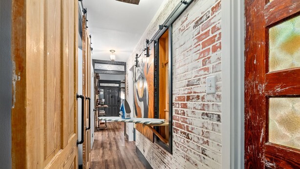 Un pasillo estrecho con puertas de madera, un muro de ladrillo y un banco de madera.