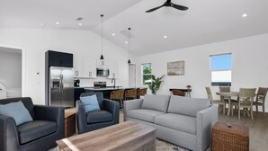 A modern living room with a grey sofa, two armchairs, a wooden coffee table, and a dining area with a table and chairs. - Harbor Place Boathouse, BRAND NEW DOCK, Open, on stilts, ocean front (Marco Island)