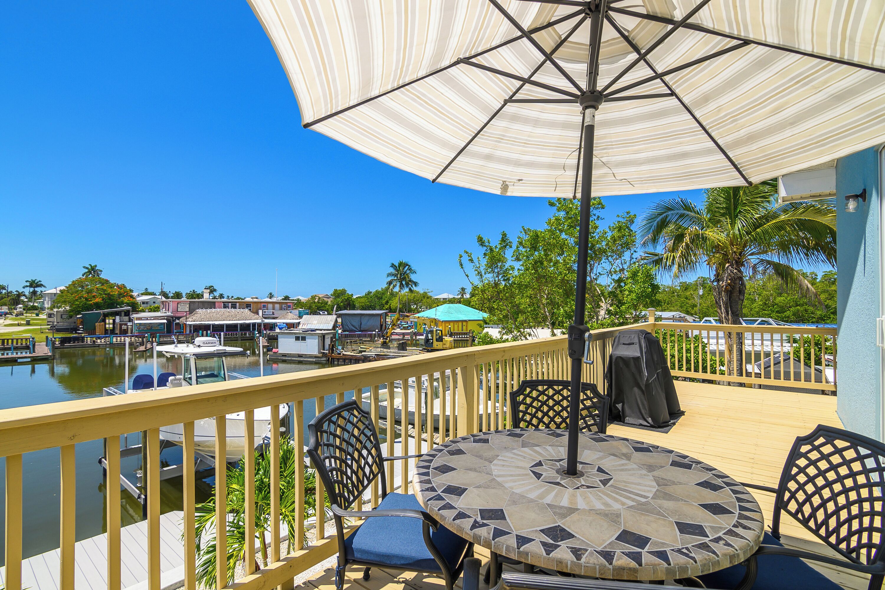 A deck with a table and chairs, overlooking a marina with boats and a clear blue sky.