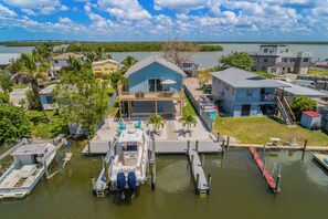 A marina with docked boats, a small house with a balcony, and a large building with a stone facade. - Harbor Place Boathouse, BRAND NEW DOCK, Open, on stilts, ocean front (Marco Island)