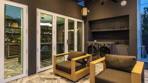 Una cucina moderna con lavatrice integrata, una porta scorrevole in vetro che dà su un patio con due sedie e un tavolo di legno.