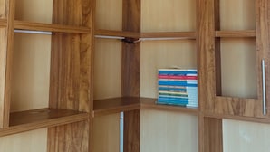 Un armadio angolare con diversi ripiani in legno e una piccola sezione con una pila di libri.