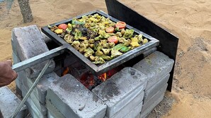 Un barbecue portable, avec des brochettes de légumes et de viande, installé sur une pile de blocs de béton.