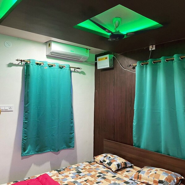 A bedroom with teal curtains, a patterned bedspread, and a ceiling fan.