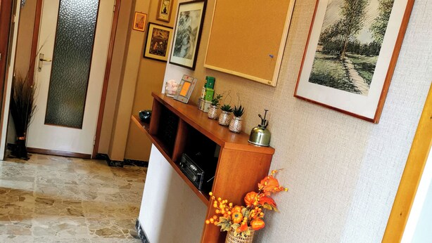 A hallway with a stone floor, a wooden reception desk, framed artwork on the walls, and a door with a frosted glass panel. - Large apartment near the lake and beach with mountain views in the greenery (Lombardia)