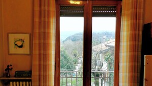 A room with a wooden door leading to a balcony, a radiator, and a small shelf with a decorative item. - Large apartment near the lake and beach with mountain views in the greenery (Lombardia)
